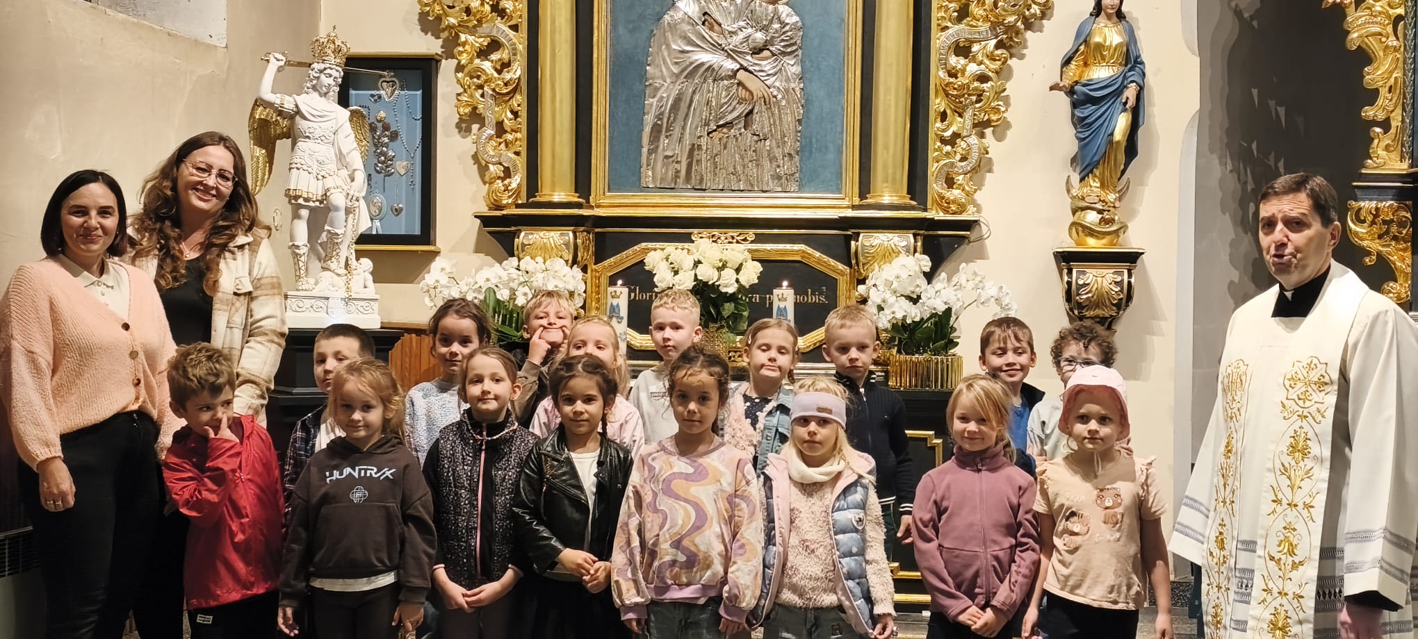 Dzieci z grupy "Motylki" wraz z księdzem proboszczem oraz wychowawcami na tle ołtarza w parafilanym kościele.